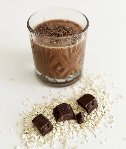 a glass filled with chocolate oat milk with oats and chocolate on the side