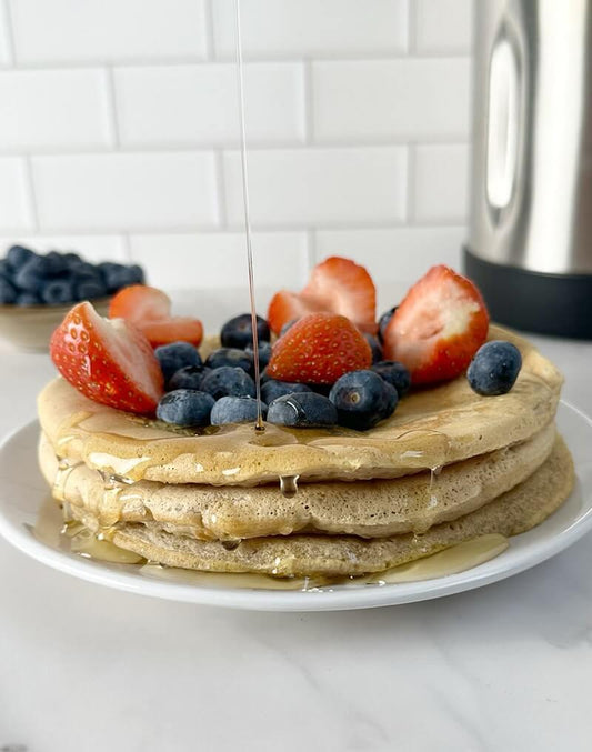 Vegan pancakes topped with fresh strawberries, blueberries, and syrup, served on a white plate